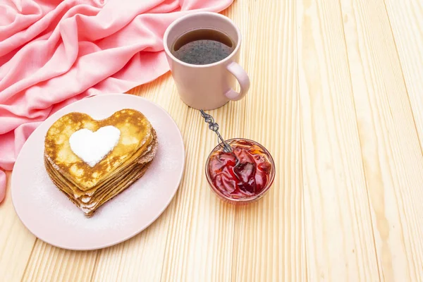 Crêpes en forme de coeur pour un petit déjeuner romantique avec confiture de fraises et thé noir. Concept de Shrovetide (carnaval). Sur fond en bois — Photo