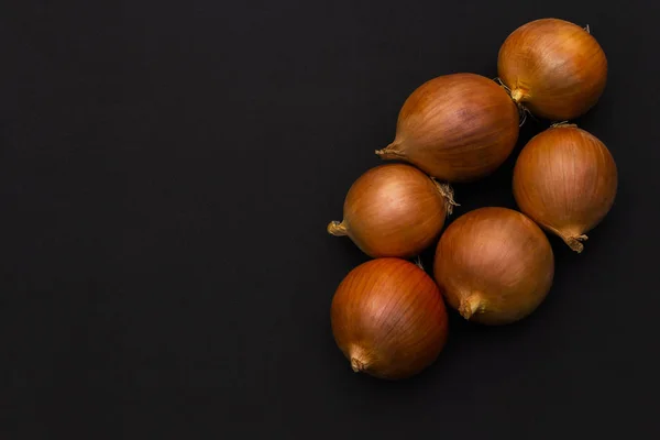 Vários grandes bulbos amarelos cebola em um fundo preto escuro. Vista superior . — Fotografia de Stock