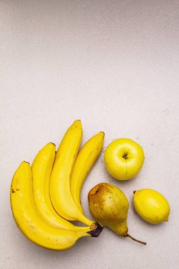 Parlak sarı meyveler. Taze muz, armut, elma, limon. Taştan bir zemin oluştur