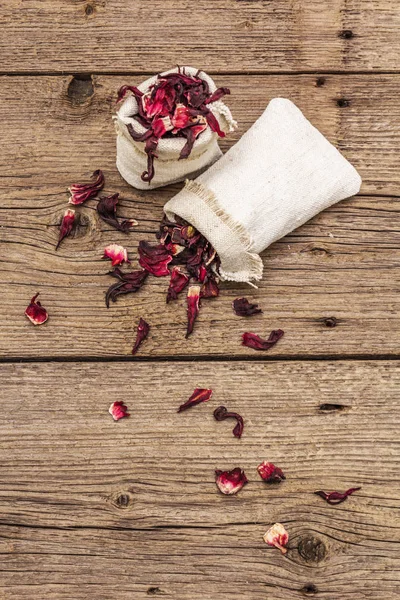Hot hibiscus tea. Dry petals, linen sacks. Healthy food and self-care concept. Old wooden boards backgrounds