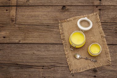 Saf ya da desi ghee (ghi), eritilmiş tereyağı. Sağlıklı yağlar kurşun geçirmez diyet konsepti veya paleo tarzı plan. Cam kavanoz, gümüş kaşık ve eski püskü kumaş. Tahta kaplama arka plan