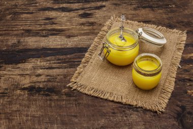 Saf ya da desi ghee (ghi), eritilmiş tereyağı. Sağlıklı yağlar kurşun geçirmez diyet konsepti veya paleo tarzı plan. Cam kavanoz, gümüş kaşık ve eski püskü kumaş. Tahta kaplama arka plan