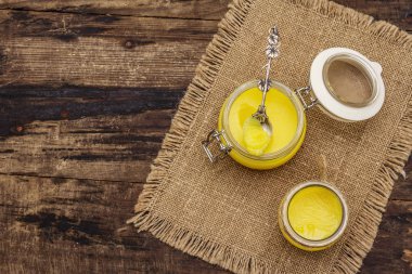 Saf ya da desi ghee (ghi), eritilmiş tereyağı. Sağlıklı yağlar kurşun geçirmez diyet konsepti veya paleo tarzı plan. Cam kavanoz, gümüş kaşık ve eski püskü kumaş. Tahta kaplama arka plan