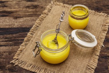 Saf ya da desi ghee (ghi), eritilmiş tereyağı. Sağlıklı yağlar kurşun geçirmez diyet konsepti veya paleo tarzı plan. Cam kavanoz, gümüş kaşık ve eski püskü kumaş. Tahta kaplama arka plan