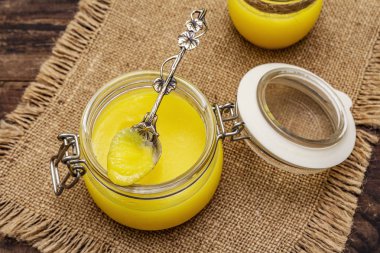 Saf ya da desi ghee (ghi), eritilmiş tereyağı. Sağlıklı yağlar kurşun geçirmez diyet konsepti veya paleo tarzı plan. Cam kavanoz, gümüş kaşık ve eski püskü kumaş. Tahta kaplama arka plan