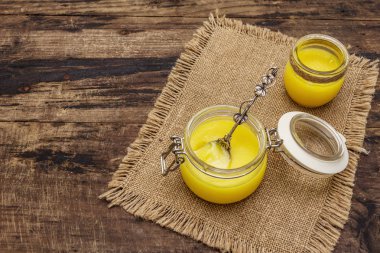 Saf ya da desi ghee (ghi), eritilmiş tereyağı. Sağlıklı yağlar kurşun geçirmez diyet konsepti veya paleo tarzı plan. Cam kavanoz, gümüş kaşık ve eski püskü kumaş. Tahta kaplama arka plan