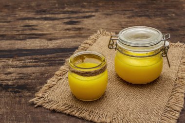 Saf ya da desi ghee (ghi), eritilmiş tereyağı. Sağlıklı yağlar kurşun geçirmez diyet konsepti veya paleo tarzı plan. Cam kavanoz, gümüş kaşık ve eski püskü kumaş. Tahta kaplama arka plan