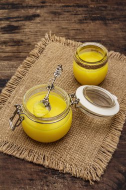 Saf ya da desi ghee (ghi), eritilmiş tereyağı. Sağlıklı yağlar kurşun geçirmez diyet konsepti veya paleo tarzı plan. Cam kavanoz, gümüş kaşık ve eski püskü kumaş. Tahta kaplama arka plan