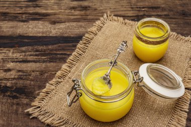 Saf ya da desi ghee (ghi), eritilmiş tereyağı. Sağlıklı yağlar kurşun geçirmez diyet konsepti veya paleo tarzı plan. Cam kavanoz, gümüş kaşık ve eski püskü kumaş. Tahta kaplama arka plan