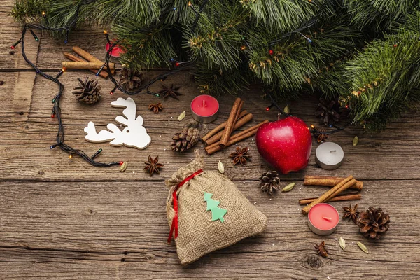 Spirit Christmas background. Gift in sack, New Year tree, apple, candles, spices, deer, cones. Nature decorations, vintage wooden boards