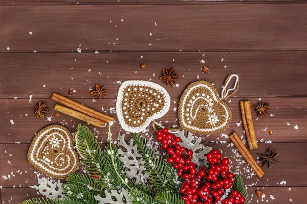 Weihnachtlicher Hintergrund. Neujahrstanne, Hundsrose, frische Blätter, gehäkelte Lebkuchenherzen, Gewürze und Kunstschnee. Holzbrettkulisse — Stockfoto