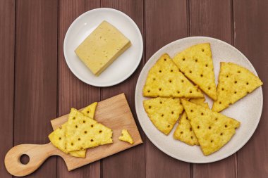 Peynirli kraker, tuzlu atıştırmalık konsepti. Kurabiyeler, bir parça peynir, kesme tahtası. Tahta arka plan