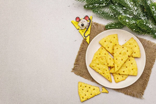 Slavnostní sýrové krekry, novoroční snack koncept. Sušenky, postava myši, větev jedle, umělý sníh, ubrus. Kamenné betonové pozadí — Stock fotografie
