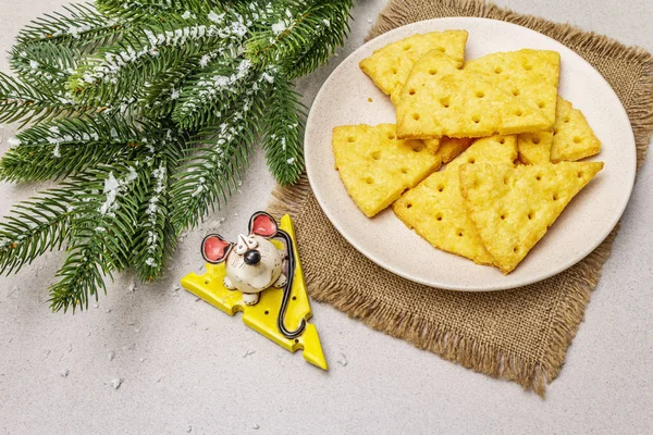 Festive cheese crackers, New Year snack concept. Cookies, mouse figure, fir tree branch, artificial snow, sackcloth napkin. Stone concrete background — Stock Photo, Image