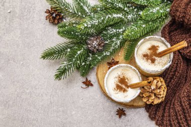 Camda tarçınlı ev yapımı eggnog. Tipik Noel tatlısı. Evergreen köknar brunch 'ı, koniler, rahat ekose kumaş, yapay kar. Taş beton arka plan