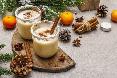 Noel ve kış tatillerinde tarçınlı yumurta likörü ve hindistan cevizi. Baharatlı bardakta ev yapımı içecek. Mandalina, mum, hediye. Taş beton arka plan