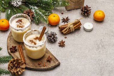 Noel ve kış tatillerinde tarçınlı yumurta likörü ve hindistan cevizi. Baharatlı bardakta ev yapımı içecek. Mandalina, mum, hediye. Taş beton arka plan