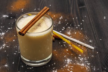 Geleneksel kışın sütlü, romlu ve tarçınlı yumurta likörü rendelenmiş hindistan cevizli. Kokteyl pipetleri, koyu ahşap arka plan