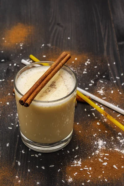 Традиционный зимний эггног с молоком, ромом и корицей, посыпать тертым мускатным орехом. Соломинки для коктейля, темный деревянный фон — стоковое фото