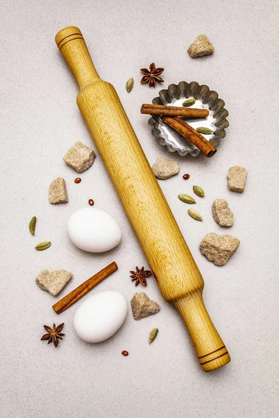 Christmas cooking background, spices, eggs, brown lump sugar, cupcake baking dish and a rolling pin. Light stone concrete background