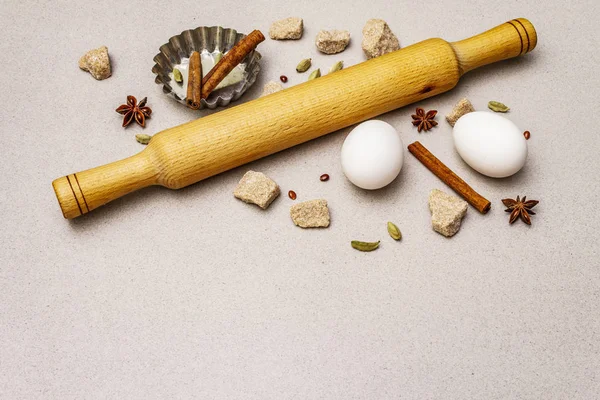 Christmas cooking background, spices, eggs, brown lump sugar, cupcake baking dish and a rolling pin. Light stone concrete background