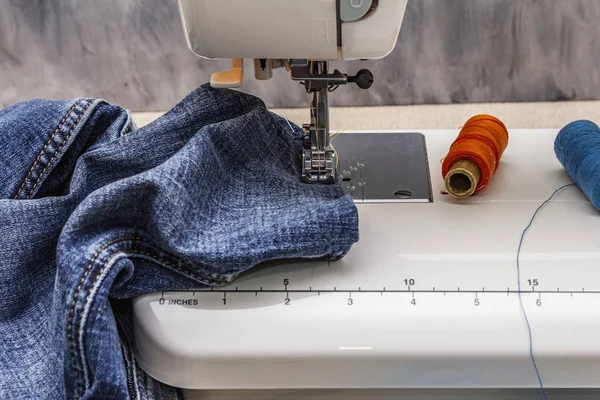 Sewing machine foot on denim. Scissors, spools of thread. Stands on a table, wooden backdrop