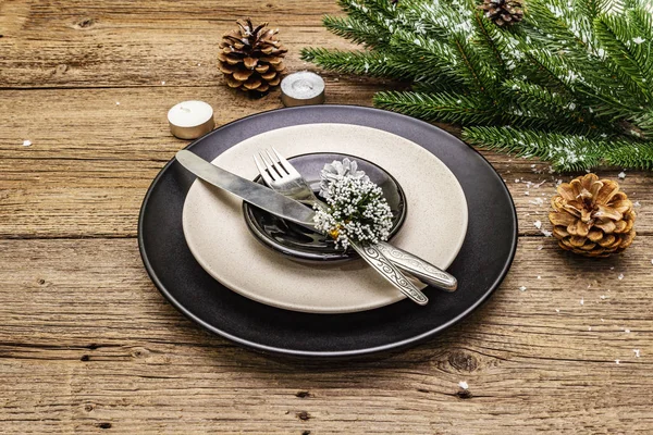 Christmas and New Year dinner place setting. Evergreen fir tree branch, candles, cones, ceramic plates, fork and knife. Winter cutlery wooden background
