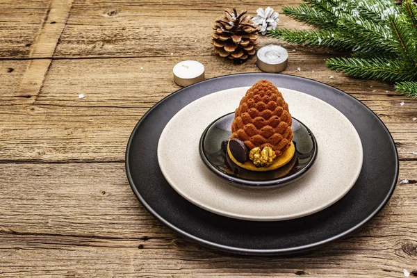 Christmas and New Year dinner place setting. Sweet snack, fir tree branch, candles, cones, ceramic plates, fork and knife. Winter cutlery wooden background