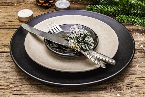 Christmas and New Year dinner place setting. Evergreen fir tree branch, candles, cones, ceramic plates, fork and knife. Winter cutlery wooden background