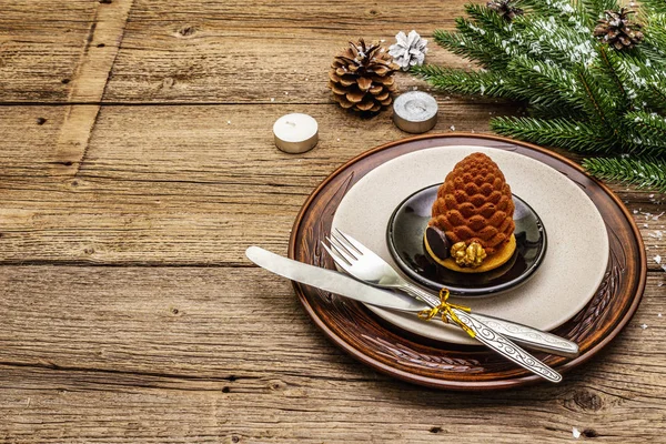 Christmas and New Year dinner place setting. Sweet snack, fir tree branch, candles, cones, ceramic plates, fork and knife. Winter cutlery wooden background