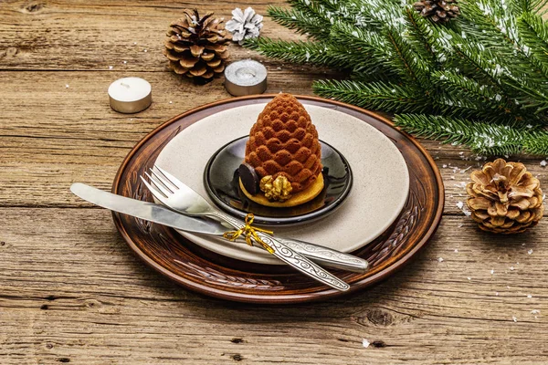Christmas and New Year dinner place setting. Sweet snack, fir tree branch, candles, cones, ceramic plates, fork and knife. Winter cutlery wooden background — Stock Photo, Image