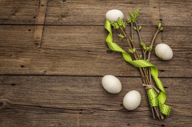 Zero waste Easter concept. Spring twigs with fresh green leaves, wooden eggs, polka dot ribbon. Old vintage wooden boards background