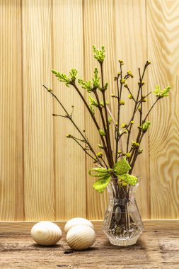 Zero waste Easter concept. Spring twigs with fresh green leaves. Glass vase, wooden eggs, polka dot ribbon. Wooden boards background and backdrop