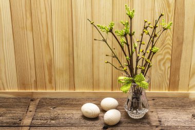 Zero waste Easter concept. Spring twigs with fresh green leaves. Glass vase, wooden eggs, polka dot ribbon. Wooden boards background and backdrop