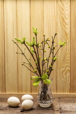 Zero waste Easter concept. Spring twigs with fresh green leaves. Glass vase, wooden eggs, polka dot ribbon. Wooden boards background and backdrop
