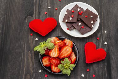 Sevgililer Günü romantik konsepti. Çikolata, taze olgun çilek, kırmızı keçeli kalp. Aşıklar için tatlı. Siyah tahta arkaplan