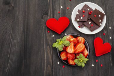 Sevgililer Günü romantik konsepti. Çikolata, taze olgun çilek, kırmızı keçeli kalp. Aşıklar için tatlı. Siyah tahta arkaplan