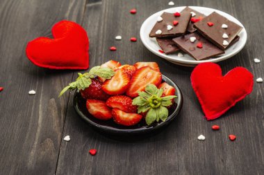 Sevgililer Günü romantik konsepti. Çikolata, taze olgun çilek, kırmızı keçeli kalp. Aşıklar için tatlı. Siyah tahta arkaplan