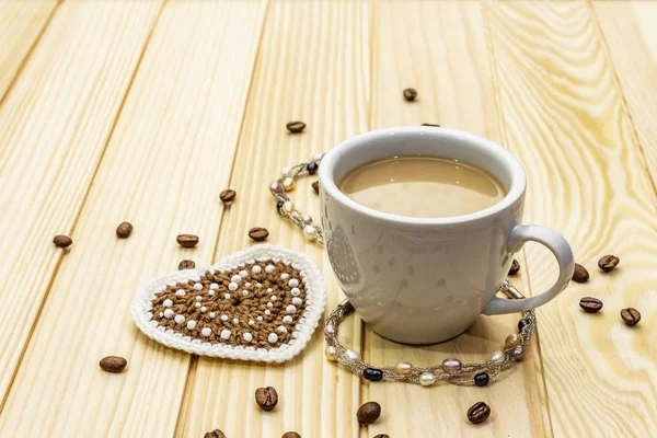 Concept de Saint-Valentin. Tasse de café, coeur tricoté, cordon de perles de perles. Petit déjeuner romantique et cadeau sur fond de planches en bois — Photo