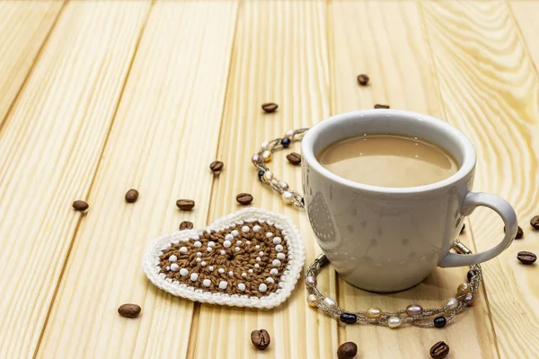Valentine\'s Day concept. Cup of coffee, knitted heart, string of pearl beads. Romantic breakfast and gift on wooden boards background
