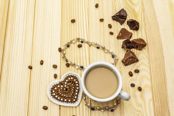 Concept de Saint-Valentin. Tasse de café, chocolat, coeur tricoté, cordon de perles de perles. Petit déjeuner romantique et cadeau sur fond de planches en bois, espace de copie — Photo