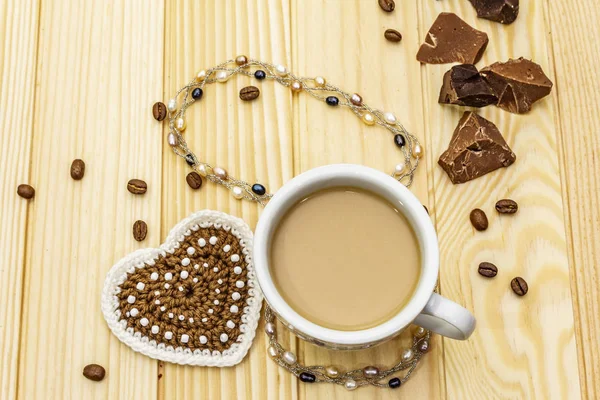 Concept de Saint-Valentin. Tasse de café, chocolat, coeur tricoté, cordon de perles de perles. Petit déjeuner romantique et cadeau sur fond de planches en bois, espace de copie — Photo