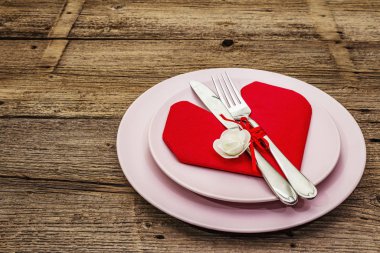 Tabaklar ve kalp şeklinde peçeteli romantik yemek masası. Sevgililer günü ya da anneler günü için aşk konsepti, düğün çatal bıçak takımı. Eski tahta kaplama arka plan