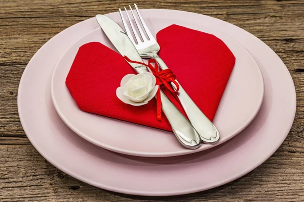 Romantic dinner table with plates and heart shape napkin. Love concept for Valentine's or mother's day, wedding cutlery. Vintage wooden boards background — Stock Photo, Image