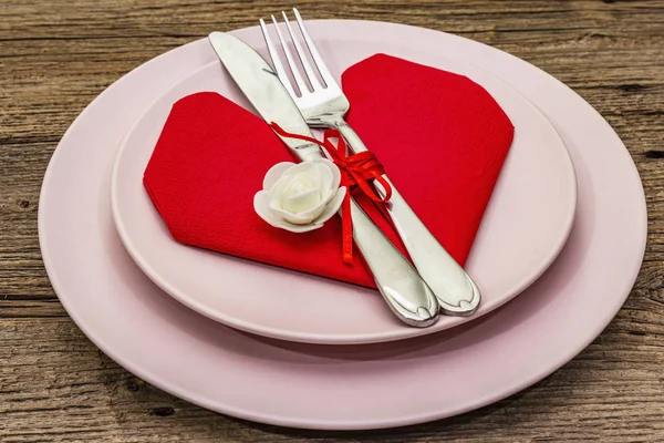 Romantic dinner table with plates and heart shape napkin. Love concept for Valentine's or mother's day, wedding cutlery. Vintage wooden boards background Royalty Free Stock Images