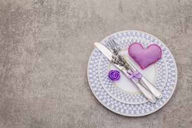 Hafif beton arka planda romantik bir masa. Sevgililer Günü ya da düğün kartı şablonu. Leylak kalp, lavanta, gül çiçeği, çatal bıçak.