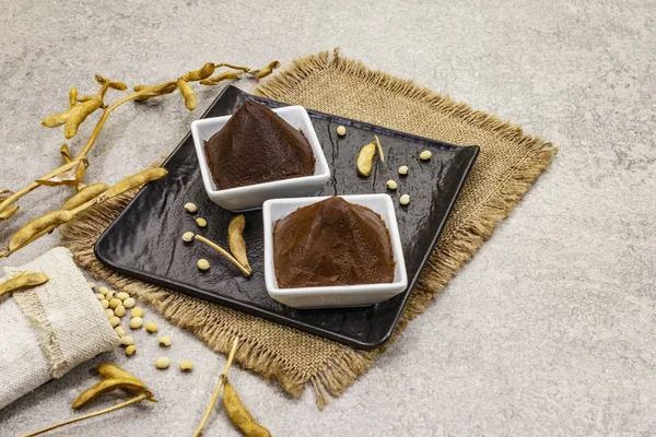 Pasta de miso, condimento tradicional japonés. Dos tipos, marrón oscuro y marrón claro con soja seca. Saco, bolsa, vainas. Fondo de hormigón piedra — Foto de Stock