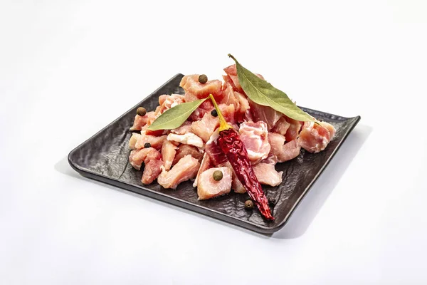 Diced raw pork meat, isolated on white background. Fresh pieces, dry bay leaf on black ceramic plate — 스톡 사진
