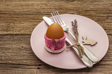 Easter table setting on vintage wooden boards background. Spring holiday card template. Cutlery, egg, lavender, bunny, knitted stand
