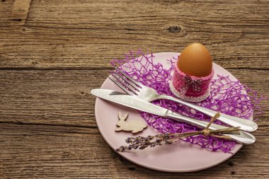 Easter table setting on vintage wooden boards background. Spring holiday card template. Cutlery, egg, lavender, bunny, knitted stand